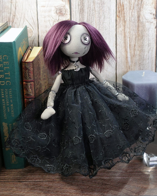 Gothic-style doll with purple hair and black lace dress in front of books and a candle.