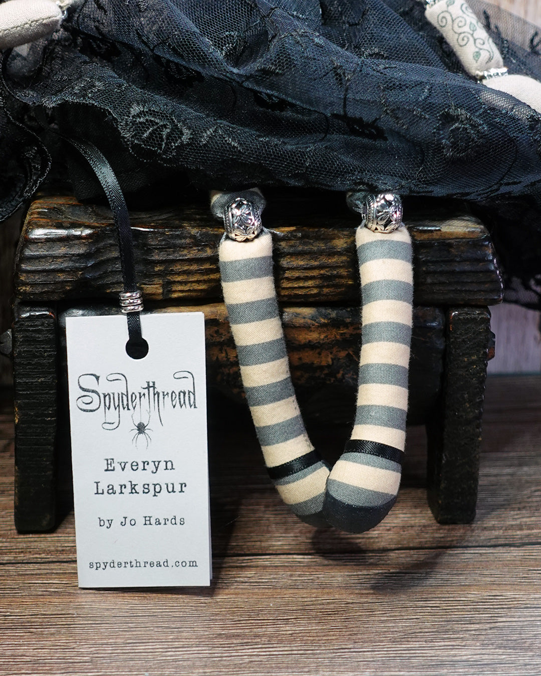 Striped doll's legs with Mary Jane shoes and silver knee joint beads next to a Spyderthread name tag on a wooden surface