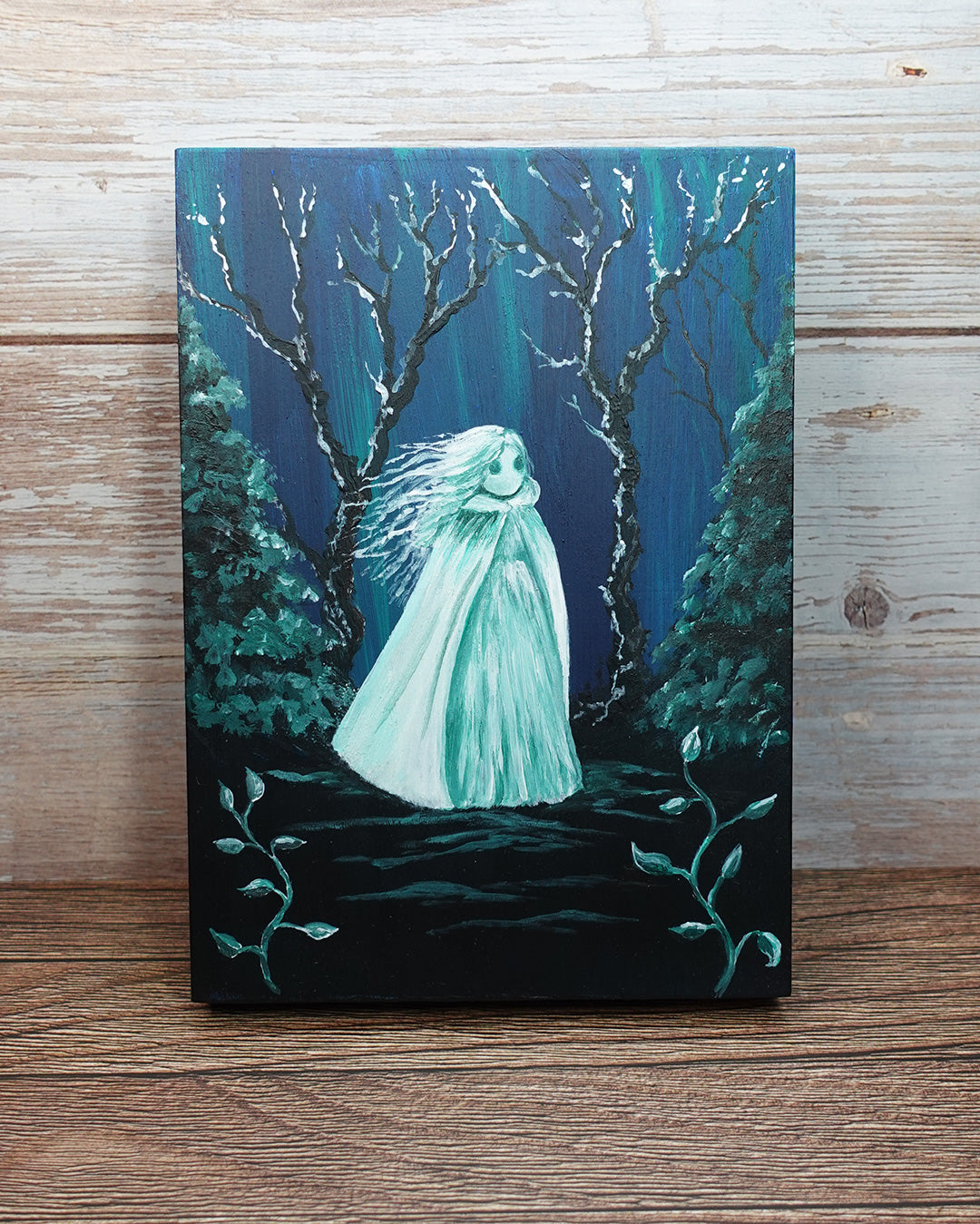 Painting of a ghostly figure in a forest with a blue green glow on a wooden surface