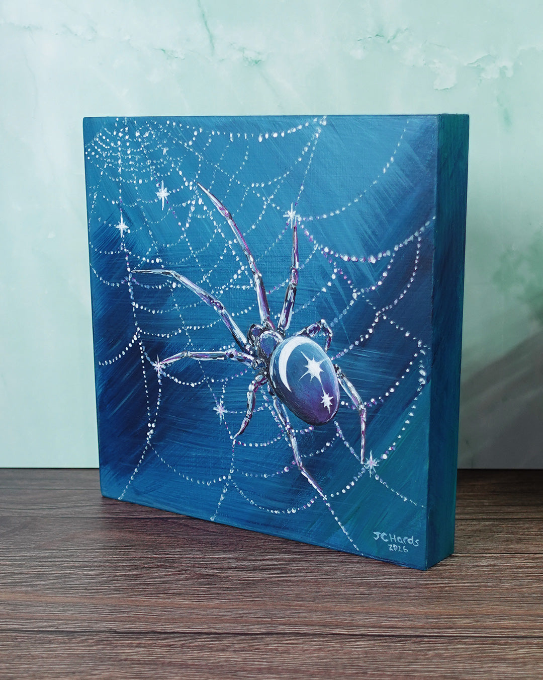a painting of a spider with moon and stars on its back in blues and purples on deep wooden panel
