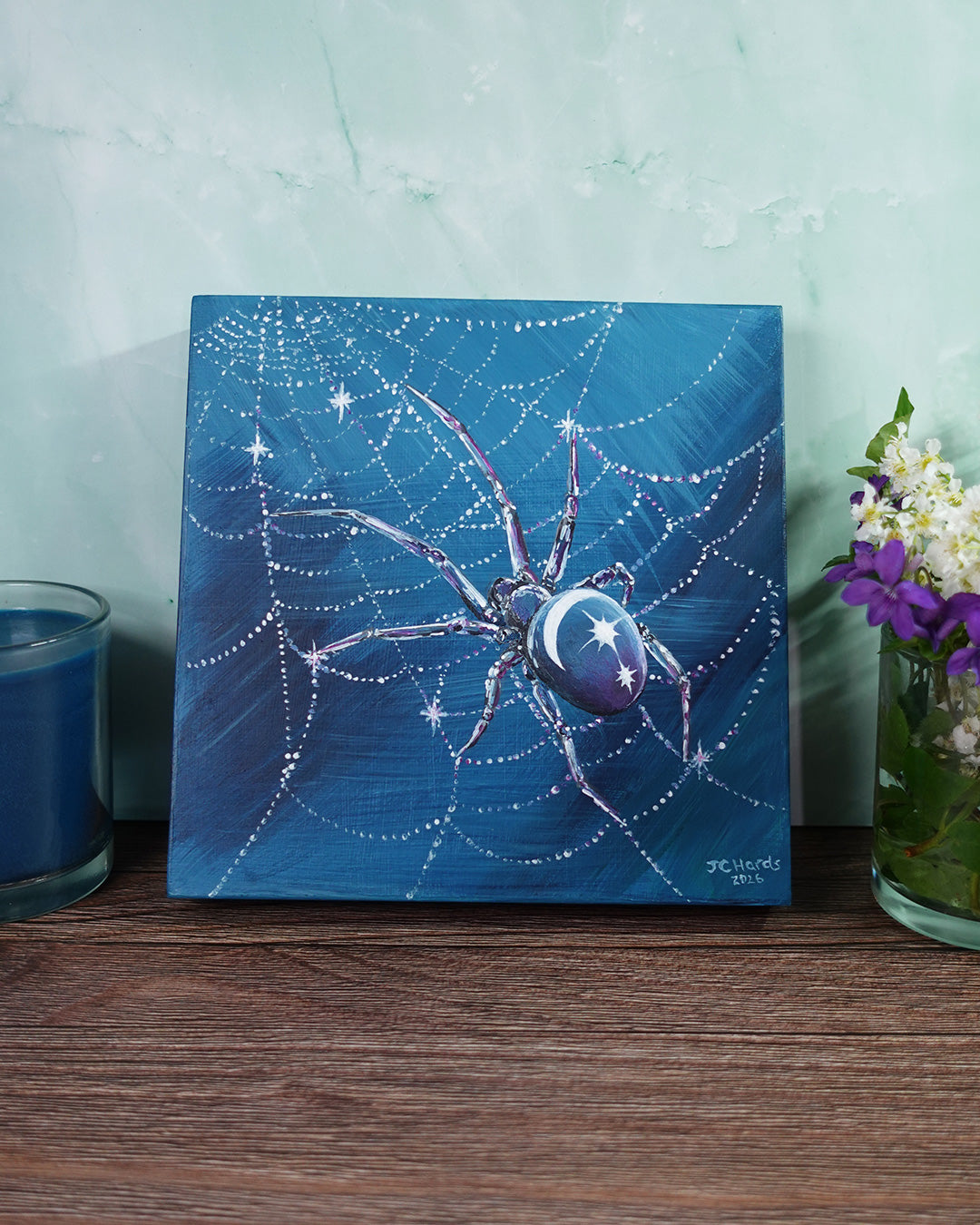 blue and purple spider painting on wooden surface with blue candle and flowers