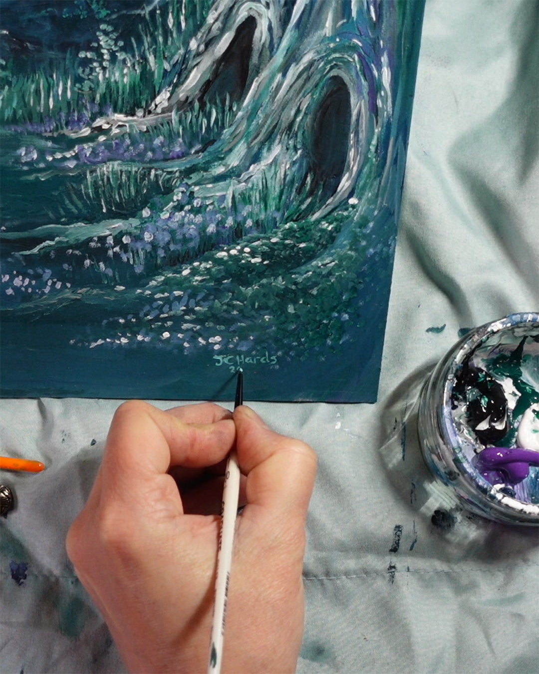 Artist's hand adding signature to bottom corner of painting