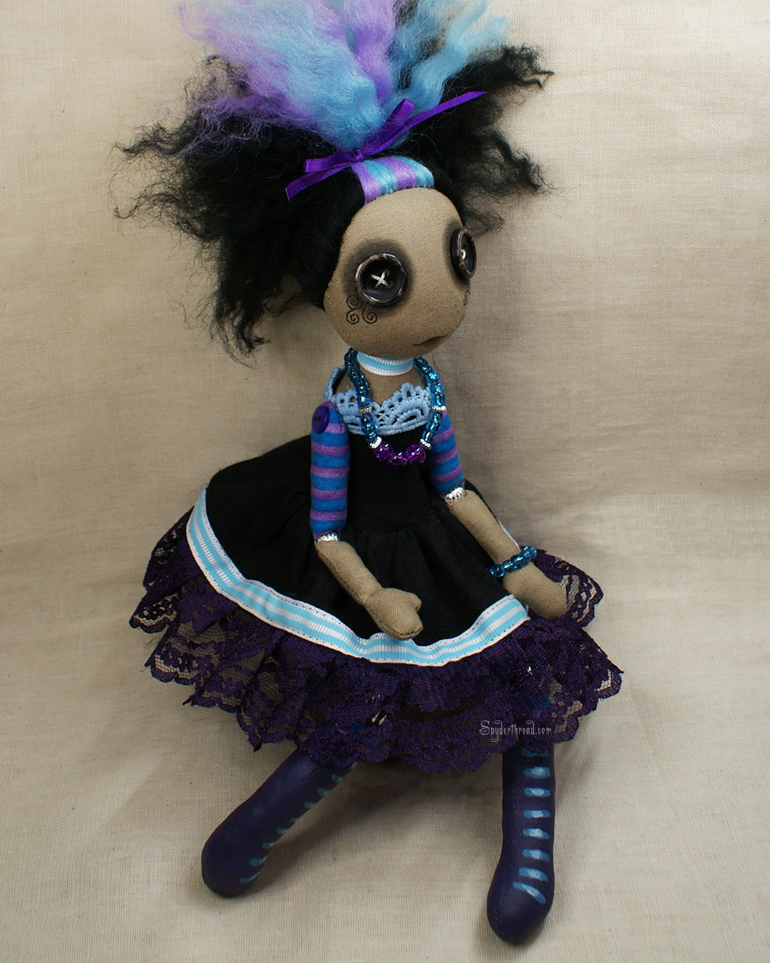 Side view of a BAME button eyed Gothic style doll in black purple and blue dress with purple lace up boots